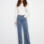 Woman wearing a white long-sleeve top and blue jeans against a white background