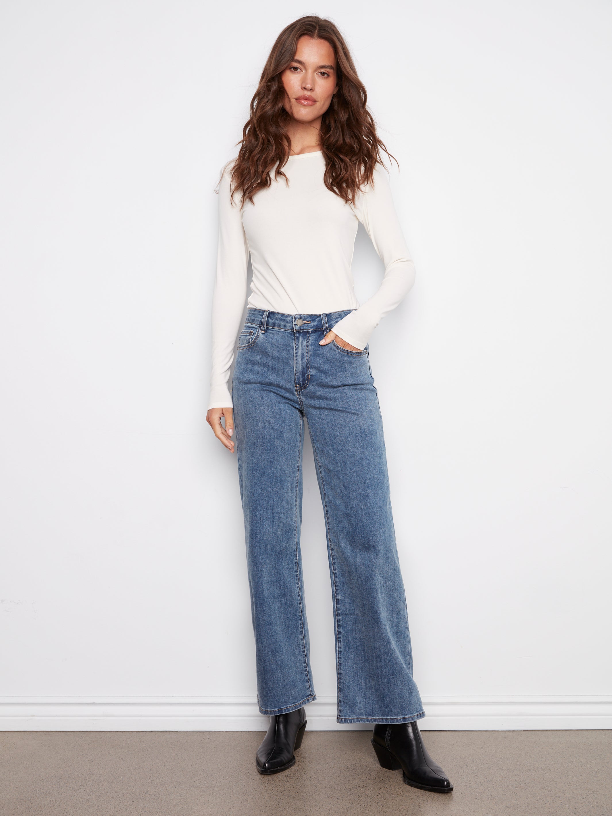 Woman wearing a white long-sleeve top and blue jeans against a white background